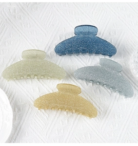 Detailed view of four glittery acrylic hair claws in blue, cream, gray, and yellow colors