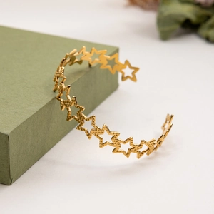 Detailed view of a gold star pattern open cuff bracelet on a dark green jewelry box