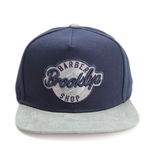 Détail de l'écusson brodé Barber Brooklyn Shop sur une casquette snapback bicolore