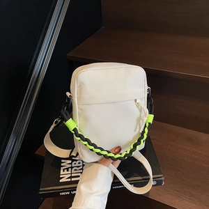 Close-up of white canvas crossbody bag featuring a green and black woven shoulder strap