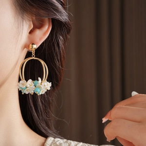 Detail of gold double-hoop earrings featuring white floral beads and blue round charms
