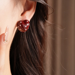 Close-up of a model wearing heart-shaped red earrings with white polka dots