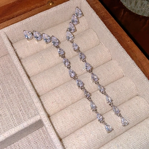 Detailed view of silver drop zirconia tassel earrings in a beige linen jewelry display case