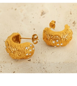 Macro shot of 18k gold-plated C-shaped earrings with inlaid crystals on stone background
