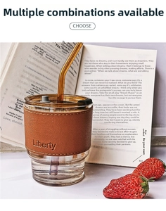 Bamboo style glass coffee cup with brown leather sleeve and amber glass straw on a book