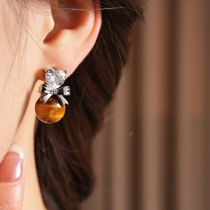 Close-up of heart zircon bow earring with brown tiger eye bead on model's ear