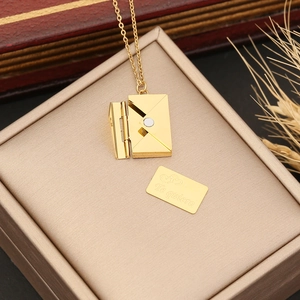 Detail of gold envelope necklace with a Te quiero engraved insert on a jewelry box