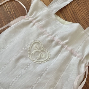 Dettaglio body neonato in pizzo bianco con fiocco rosa e ricamo a cuore sulla parte frontale