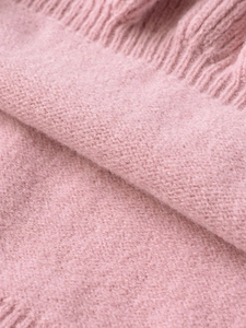 Macro shot of soft pink knitted fabric texture with delicate fringe and tassel details