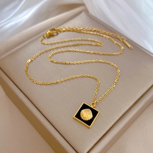 Macro detail of gold titanium necklace with black square pendant and shell emblem