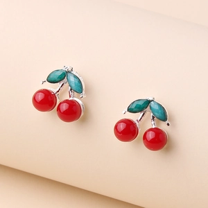 Creative cherry stud earrings with red glossy fruits and green crystal leaves on a beige base