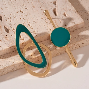 Gros plan de boucles d'oreilles asymétriques dorées à l'émail vert sur texture pierre