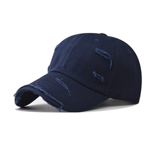 Close-up of distressed detailing and frayed holes on a navy blue washed cotton baseball cap