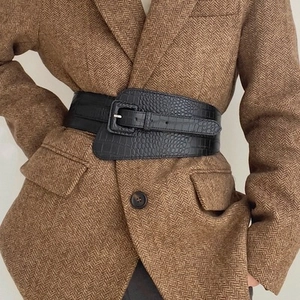 Macro detail of wide black crocodile pattern elastic belt on a herringbone blazer