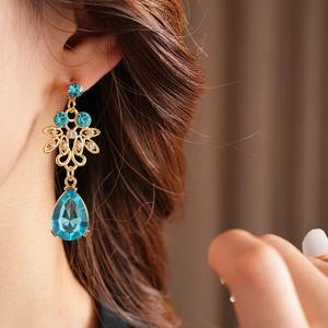 Close-up of model wearing gold flower earrings with blue teardrop stones and zircon tassels