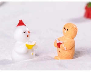 Miniature resin figurines of a snowman and gingerbread man reading on artificial snow