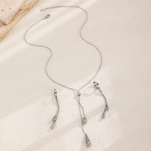 Macro detail of silver teardrop pendant necklace and matching drop earrings on stone