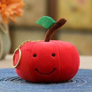 Dettaglio di un portachiavi a forma di mela rossa in peluche con viso e anello dorato