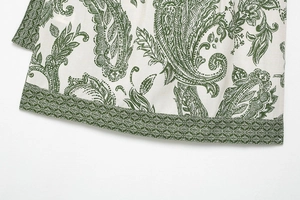 Detailed view of green paisley print and fine stitching on the white shirt hem