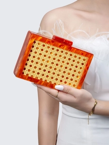 Close-up of amber acrylic frame and woven texture evening clutch held by a model