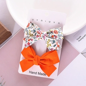 Floral fabric and solid orange bow hair clips set on a display card for girls