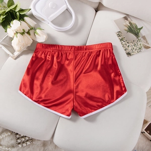 Detailed view of red silk satin lounge shorts with white piping on a soft background