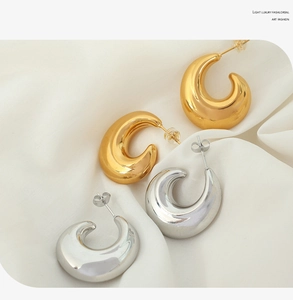 Polished gold and silver hollow C-shaped earrings on soft beige silk background