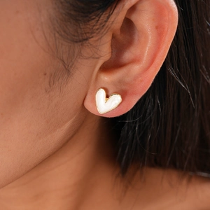 Close-up of a minimalist heart-shaped earring with golden edges and white enamel finish