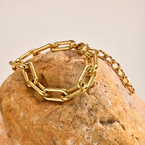 Close-up of 18K gold-plated stainless steel Figaro bracelet on a textured rock stone