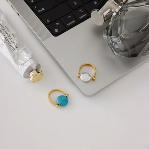Close-up of gold stainless steel rings with turquoise and pearl on a laptop background