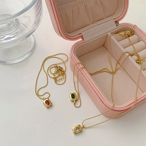 Detailed view of vintage gold bead chain necklaces with red, green, and white pendants
