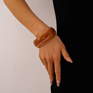 Detail of a wide amber-textured acrylic bangle with geometric design on a model wrist