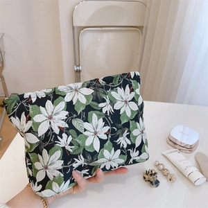 Flat makeup pouch with white floral and green leaf pattern on a black canvas texture