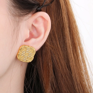 Close-up of golden square earrings with woven texture and crystals on female model