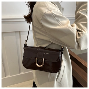 Detail of dark brown patent leather shoulder bag with metallic horseshoe buckle on a model