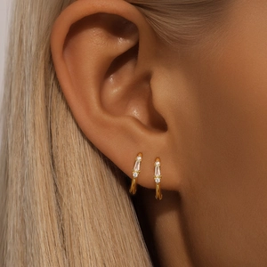Close-up of gold huggie hoop earrings with rectangular and round cubic zirconia stones