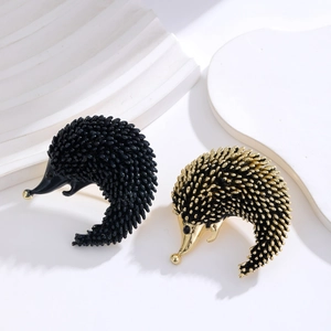 Cute enamel hedgehog brooches in black and gold finish displayed on white stone background