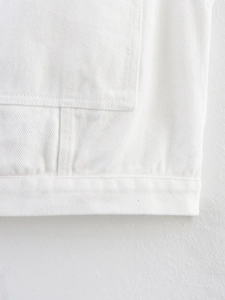 Detail of white denim vest showing stitching quality on pocket edge and hemline