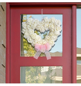 Gros plan d'une couronne de roses blanches en forme de cœur avec un nœud rose sur porte