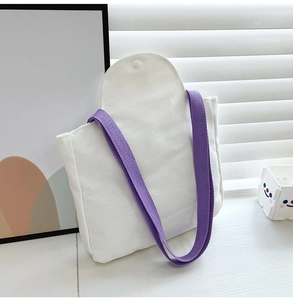 Detail of white canvas tote bag featuring purple straps and secure snap button closure