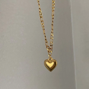 Detail of gold heart pendant on a Figaro chain made of durable titanium steel necklace
