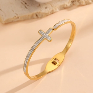Macro detail of a 18K gold-plated cross bangle with pavé zircons and shell inlay