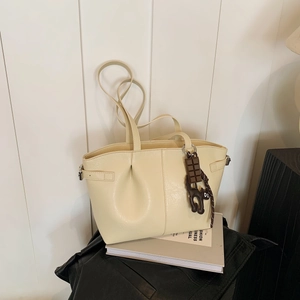 Minimalist beige pleated tote bag with chocolate charm on a white textured background