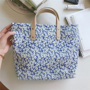 Close-up of blue floral tote bag with brown leather handles on a white wooden table