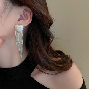 Detail of elegant heart-shaped earrings with long V-shaped tassels and brushed metal finish