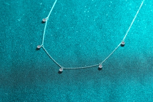 Macro shot of silver S925 necklace with five round moissanite stones on blue glitter background