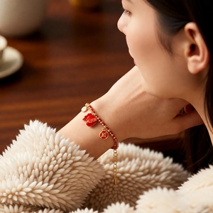 Detail of red braided lucky charm bracelet with gold koi fish and coin pendants on wrist