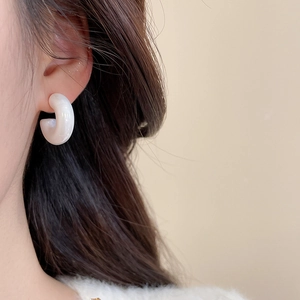 Detailed view of white acrylic C-shape earring with marble texture on a model