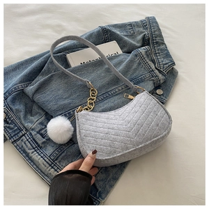 Détail du sac sous l'aisselle en feutre gris avec chaîne dorée et pompon blanc