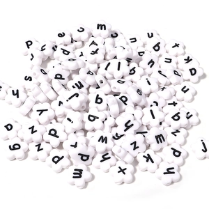 Macro detail of white flower-shaped acrylic beads with black lowercase letters for DIY jewelry